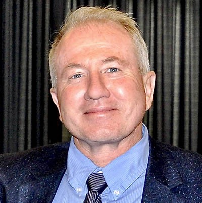 Headshot of Todd Hugie in front of dark curtain